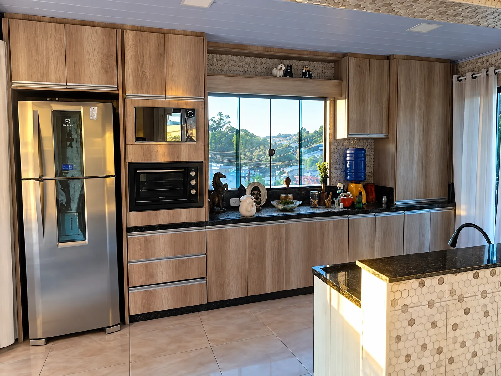 Cozinha em madeira com armários ao redor da geladeira, nicho para forno e micro-ondas e janela