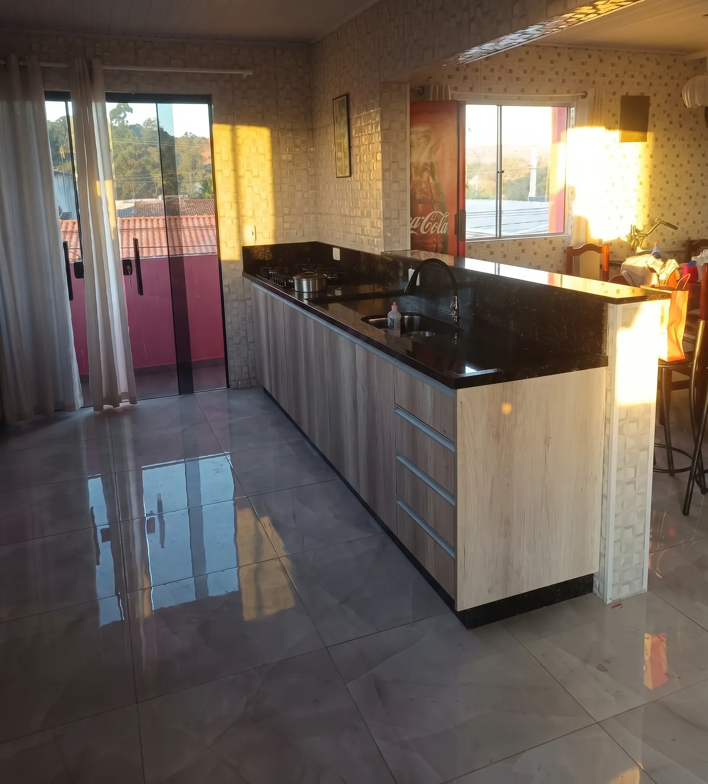 Cozinha com armários em madeira, bancada de pedra escura com cooktop e balcão de apoio