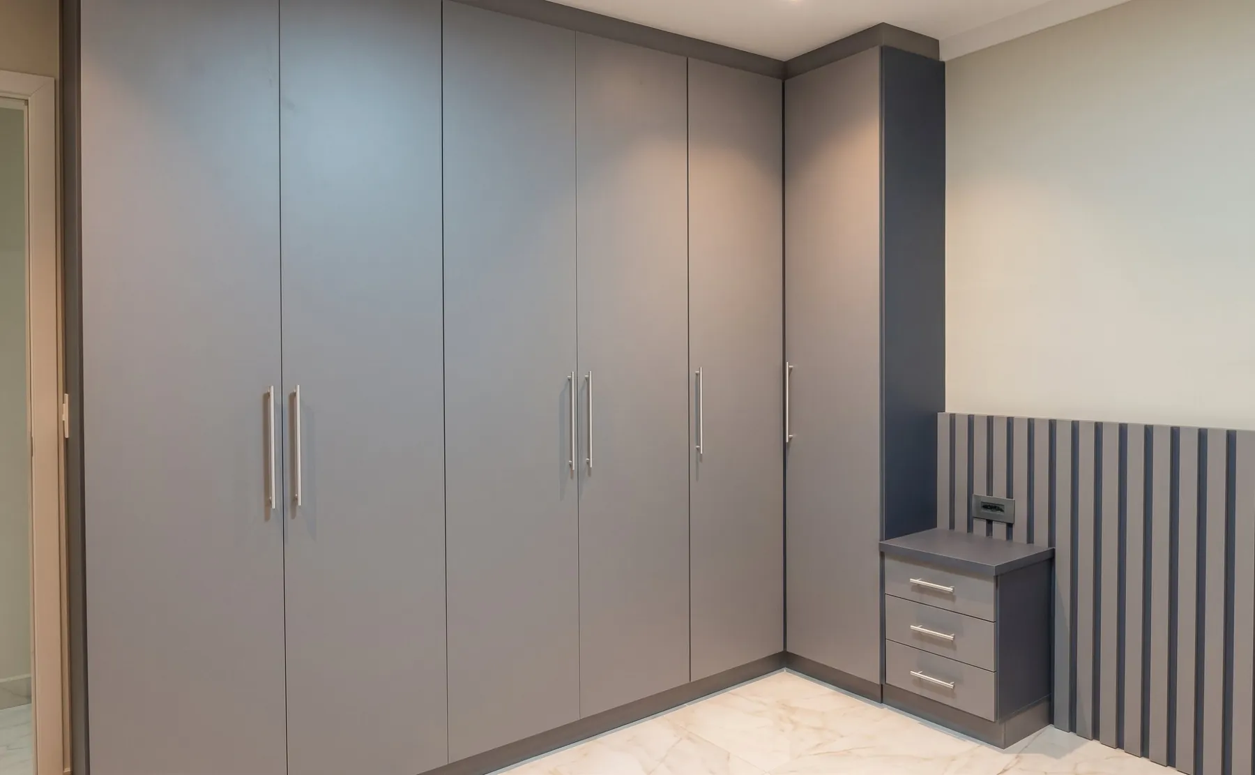 Quarto com guarda-roupa de portas cinza, criado-mudo com gavetas e painel ripado